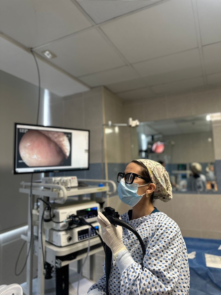 Dra. Carolina Garza con gorro, cubrebocas y guantes, sosteniendo el instrumento junto al equipo de endoscopia.